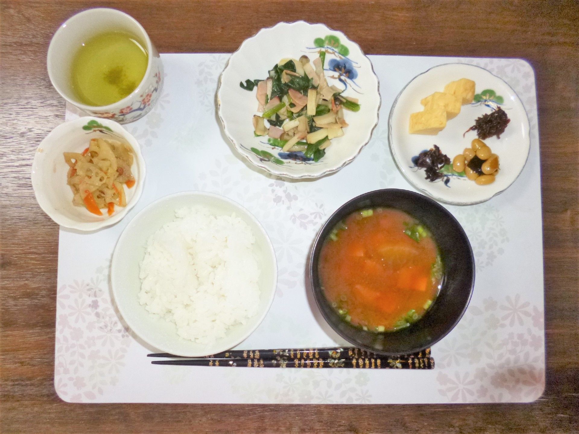 ピンク色のランチョンマットの上にご飯、お味噌汁、卵焼き、煮豆などが乗っている