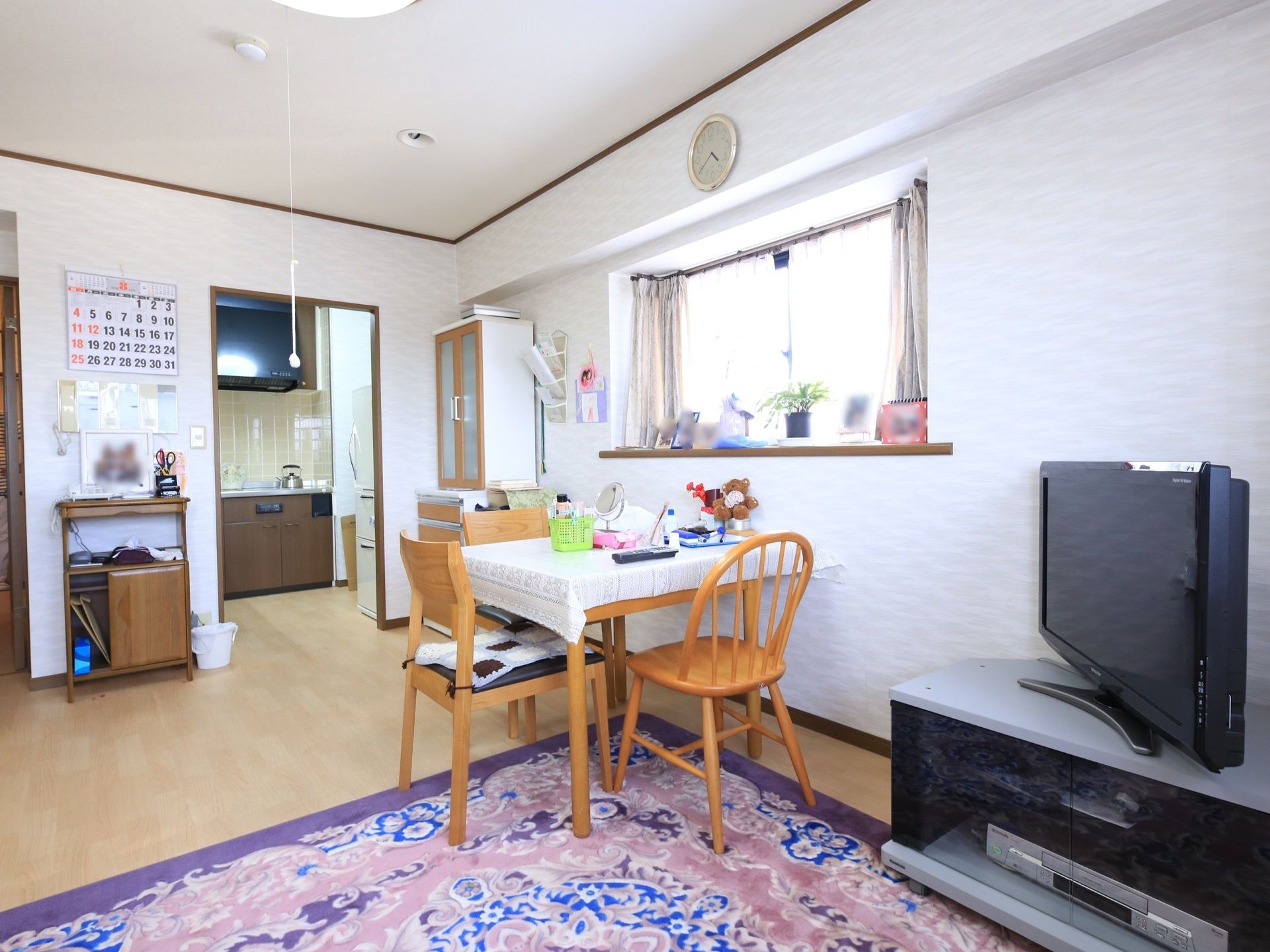日当たりの良い居室で、奥にキッチンスペースがある。リビングにはダイニングテーブルやテレビが置かれている。