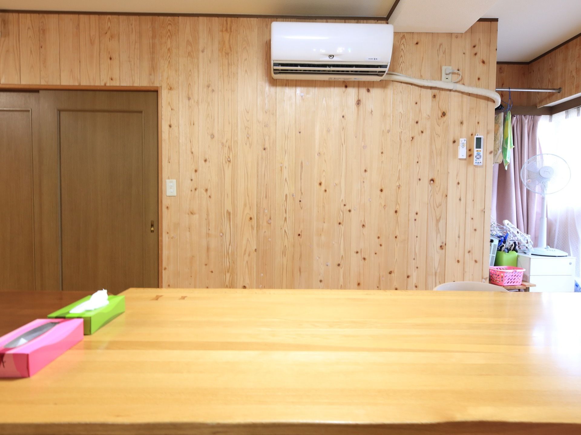 木のテーブルが設置されており、上に箱ティッシュが置かれている。壁にはエアコンが取り付けられており、奥には扇風機を用意。