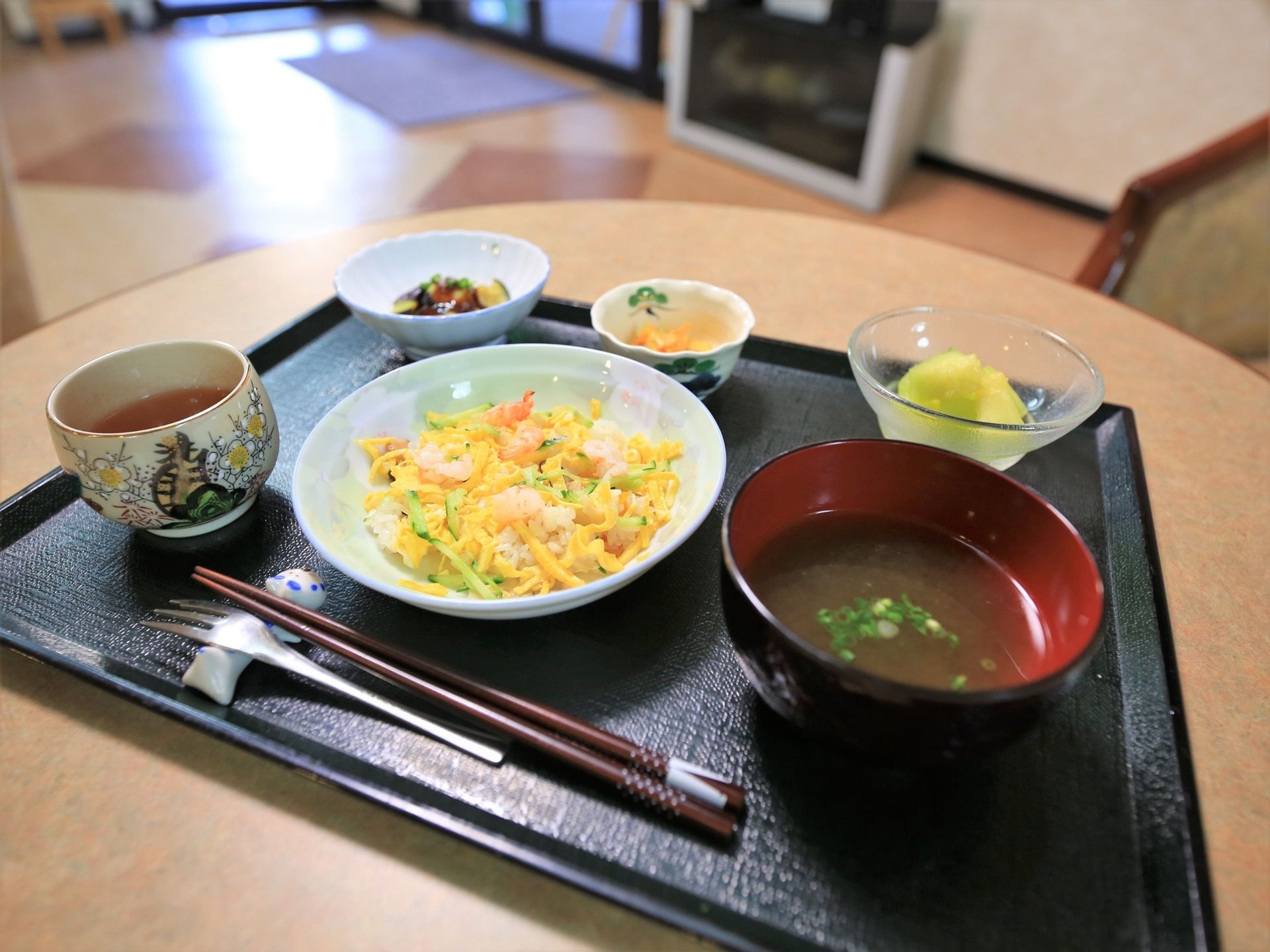 黒いトレーの上に１食分の食事が並べられている。ご飯や汁物、おかず２品とデザート、お茶が置かれている。