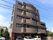 マンションのような外観の５階建ての建物である。施設前に車が複数台停められており、玄関横に自転車が１台停められている。