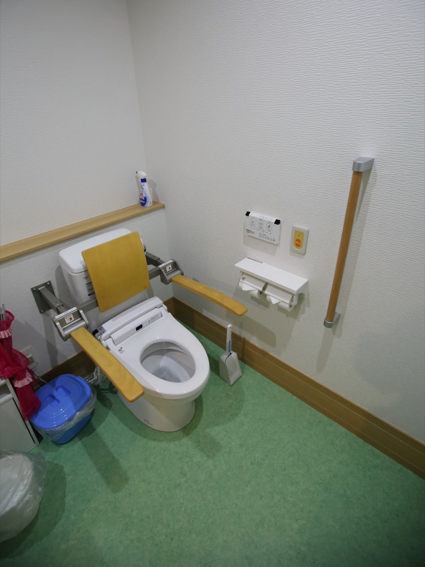 グリーンの床色が、印象的な洋式トイレである。便座の両側に手すりが備えられている。背もたれ用のクッションもある。