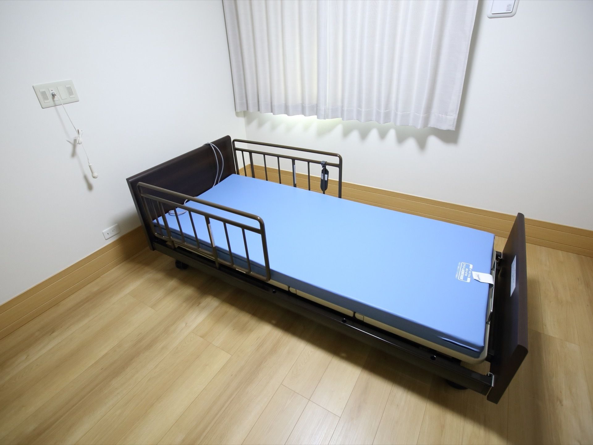 フローリング仕様の居室である。ブルーのマットが設置された、介護専用ベッドが備えられている。サイドガードもある。