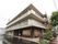 ブラウンを基調とした３階建ての建物である。施設入口には表札が設置されており、花壇には複数の種類の花が植えられている。