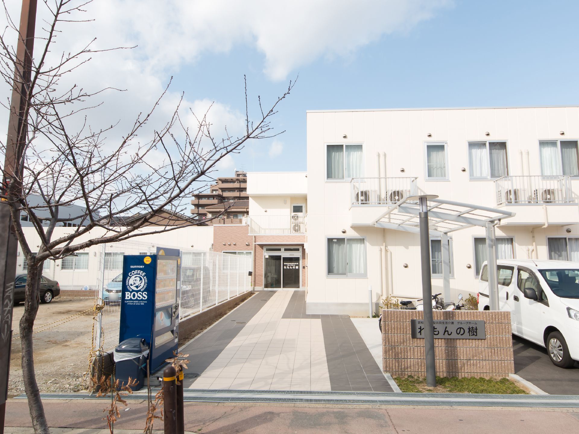 白色を基調とした外壁の２階建て施設である。歩道から玄関までタイル敷きの通路になっていて、飲料の自動販売機が置かれている。