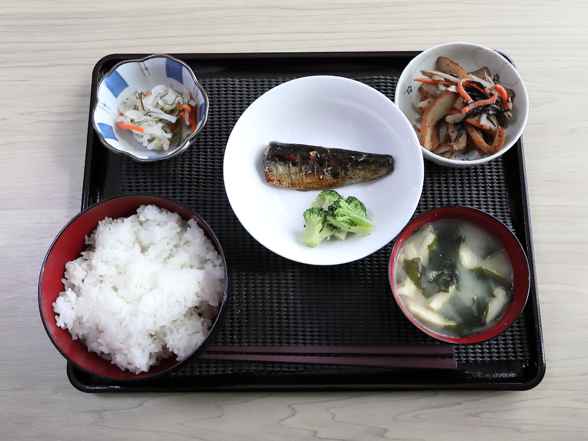 黒いプレートに、ご飯、みそ汁の他、焼き魚をはじめとしたおかずが３皿のっている。手前の方に箸が置かれている。