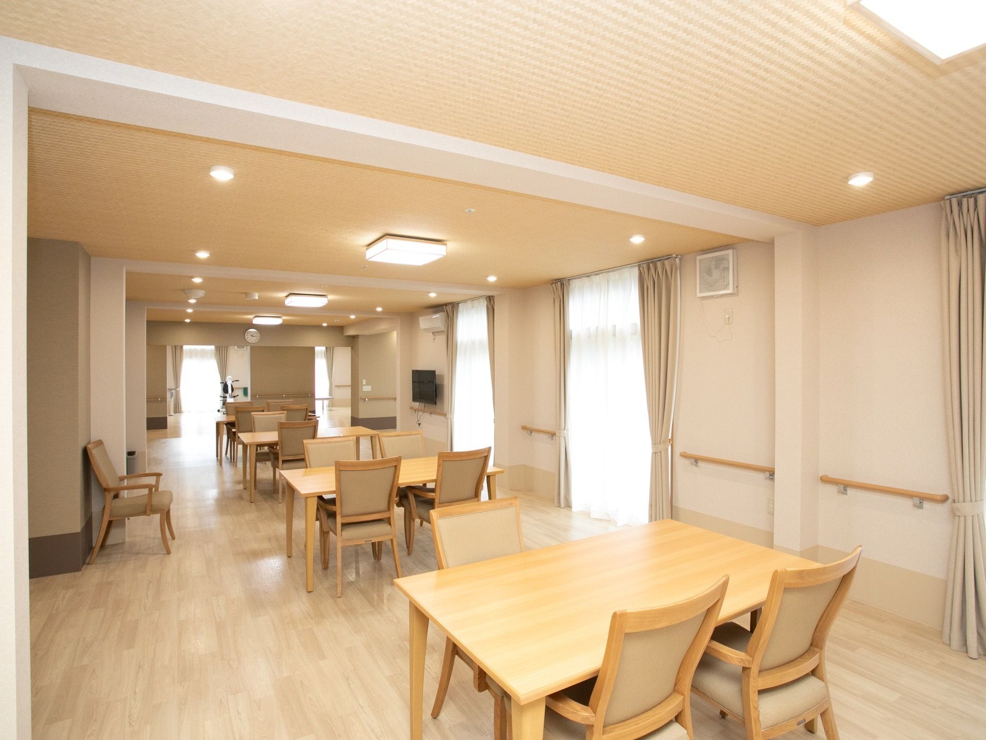 食堂の右側に壁掛けテレビがあり、その上にはエアコンも備え付けられている。奥には機能訓練スペースがある。
