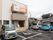 ３階建てのマンションタイプの建物。前が駐車スペースになっていて、車が4台停まっている。周りには戸建て住宅が多い。