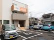 ３階建てのマンションタイプの建物。前が駐車スペースになっていて、車が4台停まっている。周りには戸建て住宅が多い。