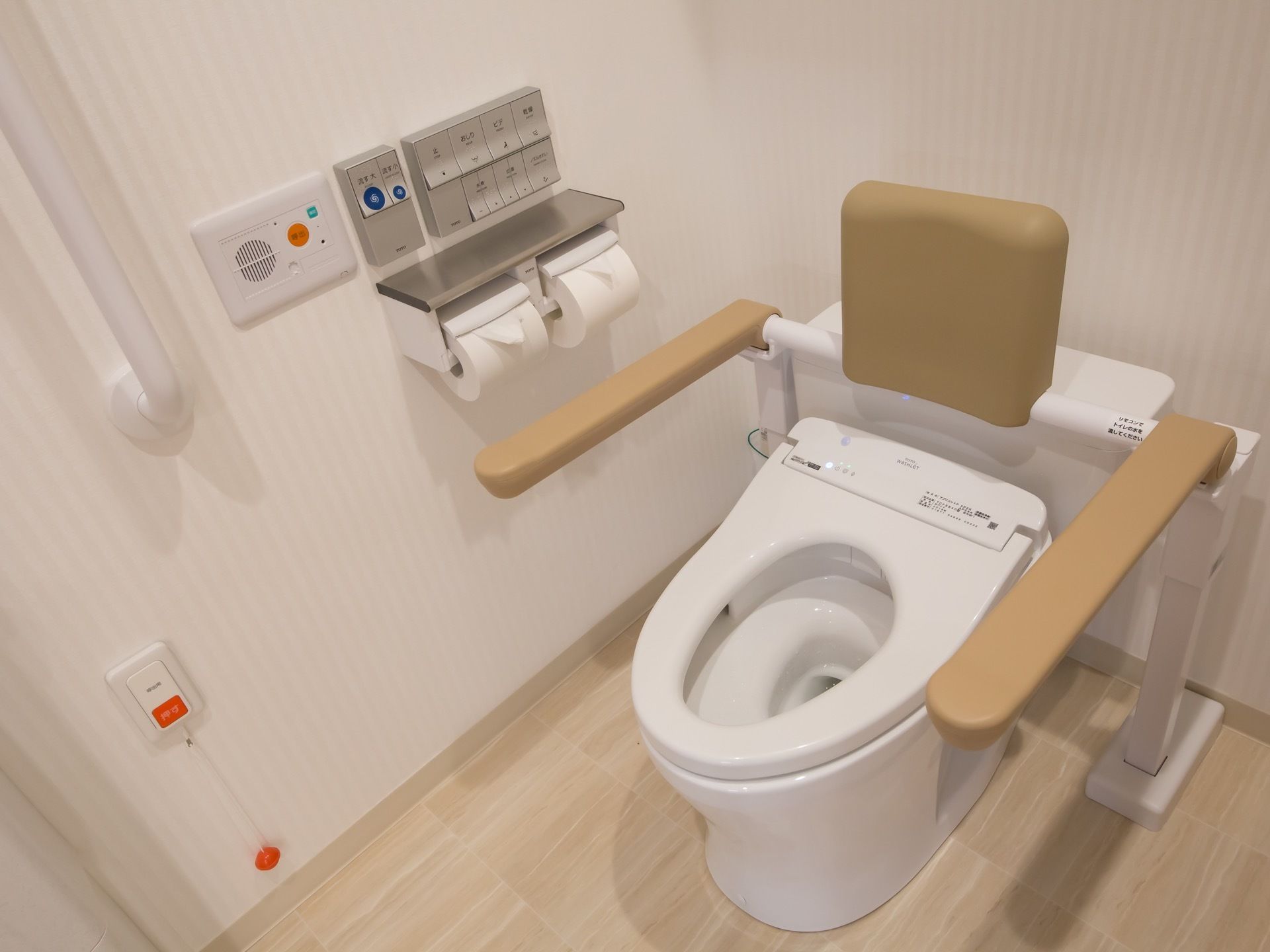 トイレの壁はストライプ柄で、ライトベージュの床を採用している。便器の両サイドに手すりが設置されている。