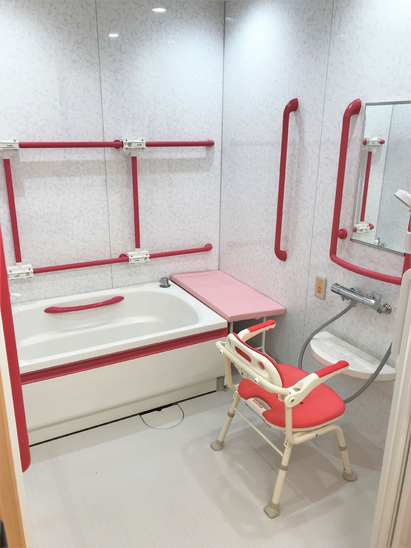 白い浴室に真っ赤な手すりが全域につき、シャワーチェアやシャワーもある。