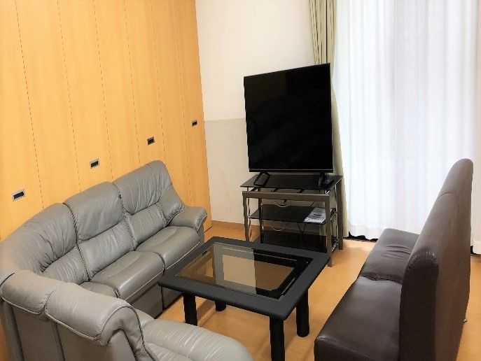 テレビ鑑賞ができるように設置された黒いソファセット。大きな窓にはカーテンがつけられている。
