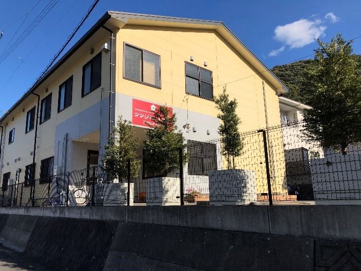 2階建ての建物はクリーム色で敷地内には木が植えられ、住宅を囲むようにフェンスが設置されている。