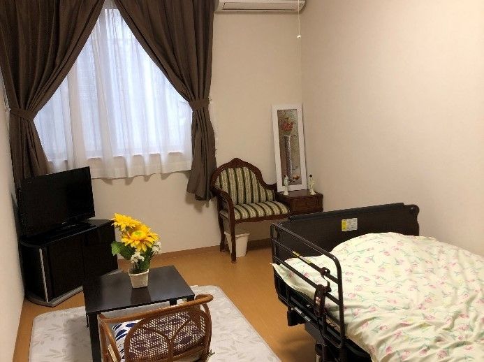 カーテンやエアコン、テレビやベッドなどの家具家電がそろった部屋。黄色いガーベラがテーブルに飾られている。