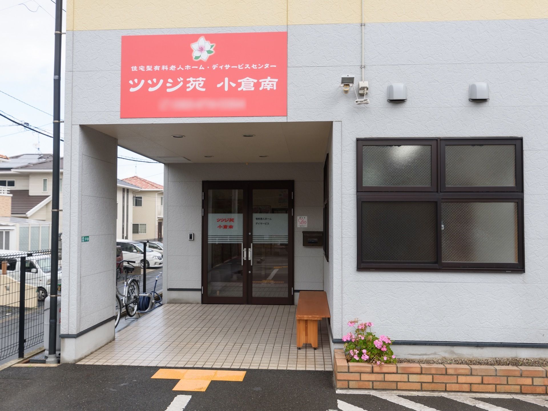 淡いベージュ色のタイル張りのポーチで、壁際にベンチが置かれている。手前の壁沿いに花壇が造られている。