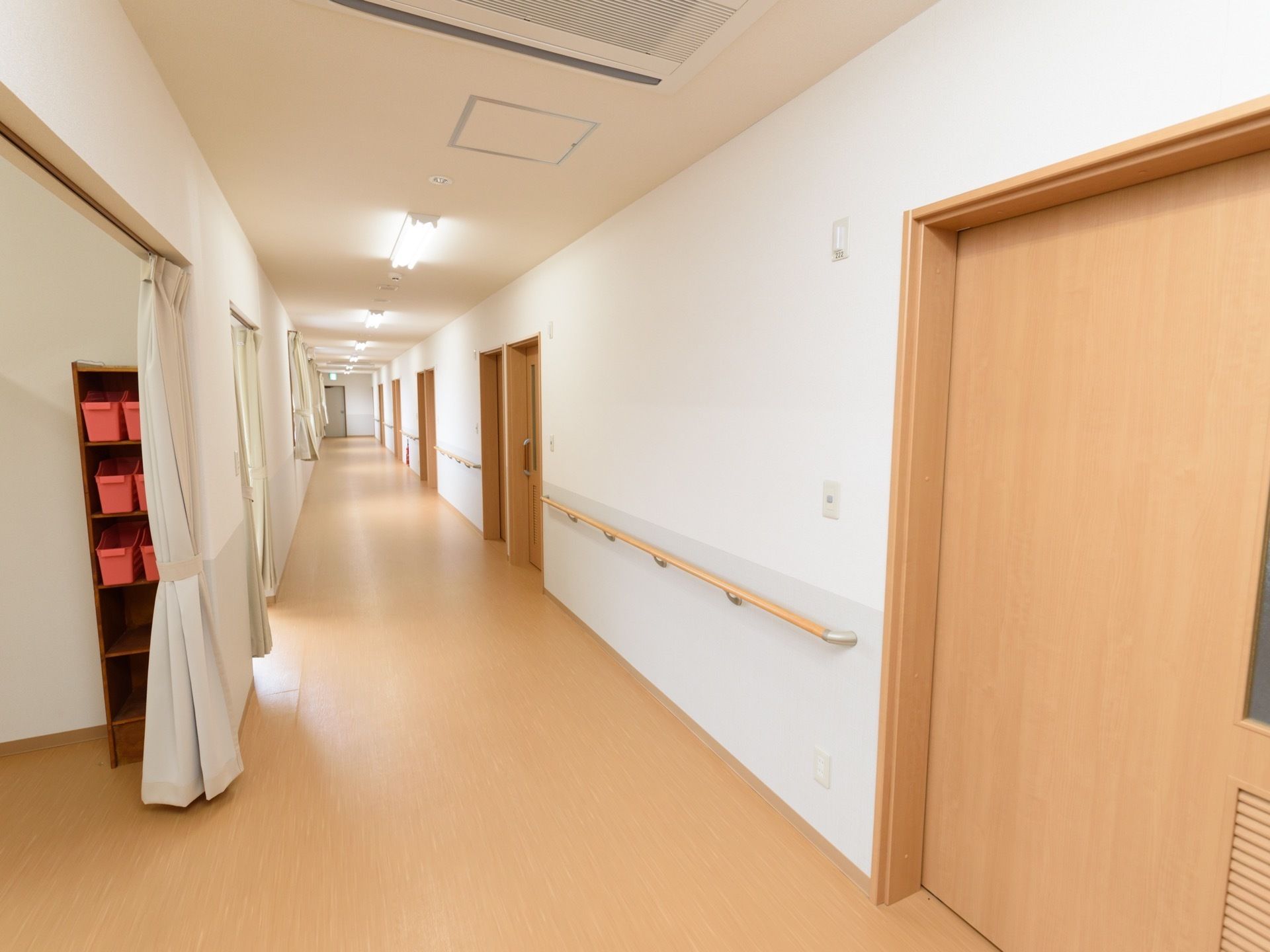 廊下の右側の壁に居室のドアと手すりが並び、左側の壁にはカーテンで仕切られた部屋が並んでいる。居室のドアはスライドドアである。