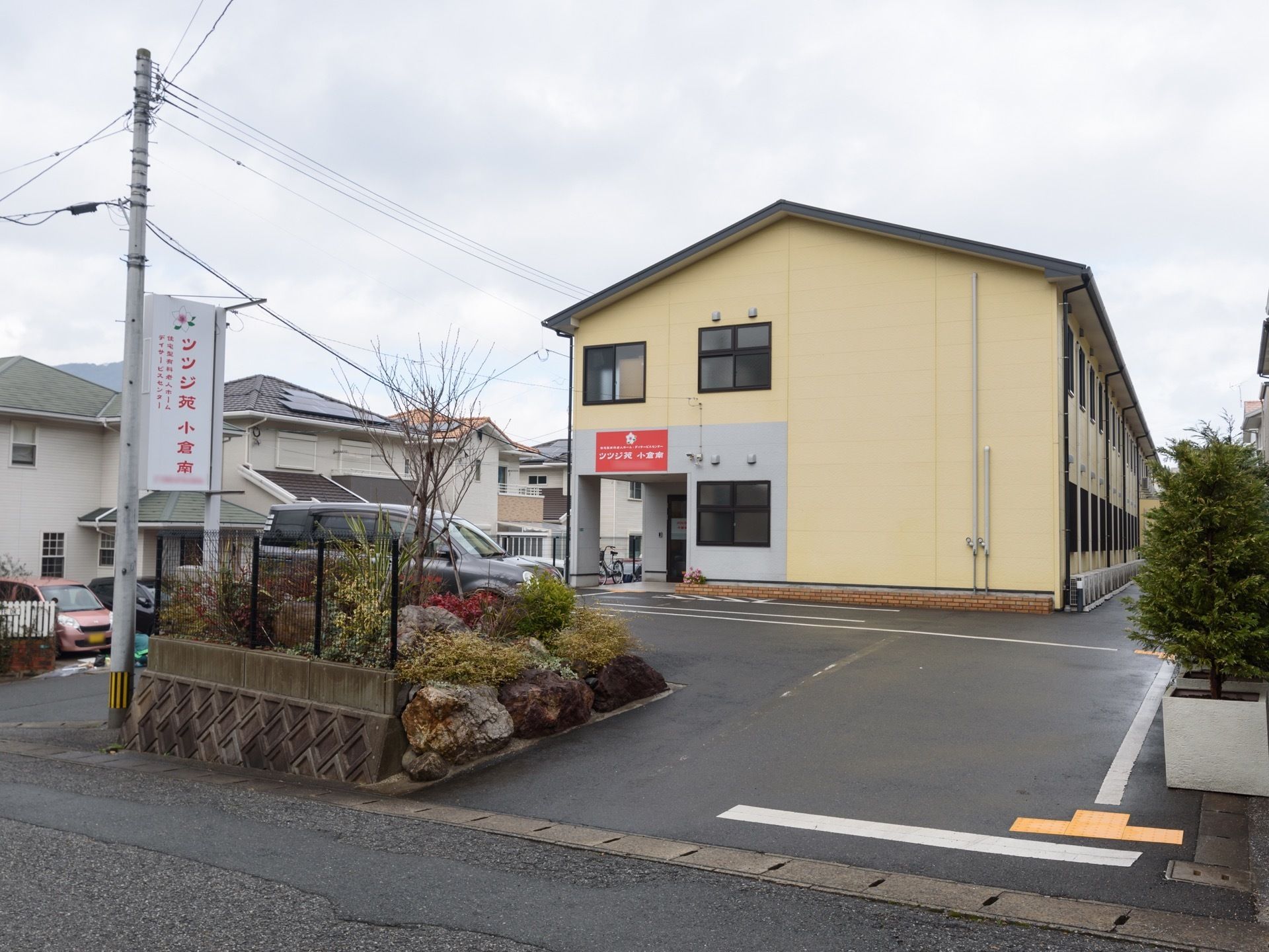 ベージュ色の外壁の、２階建ての建物である。玄関周りの壁は淡いグレーで、大きなオレンジ色の看板がかかっている。
