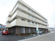下部分が茶色、上部分が白いタイル張りの４階建ての大きな建物がある。外付けの非常階段が設置されている。手前と横部分は駐車スペースになっている。
