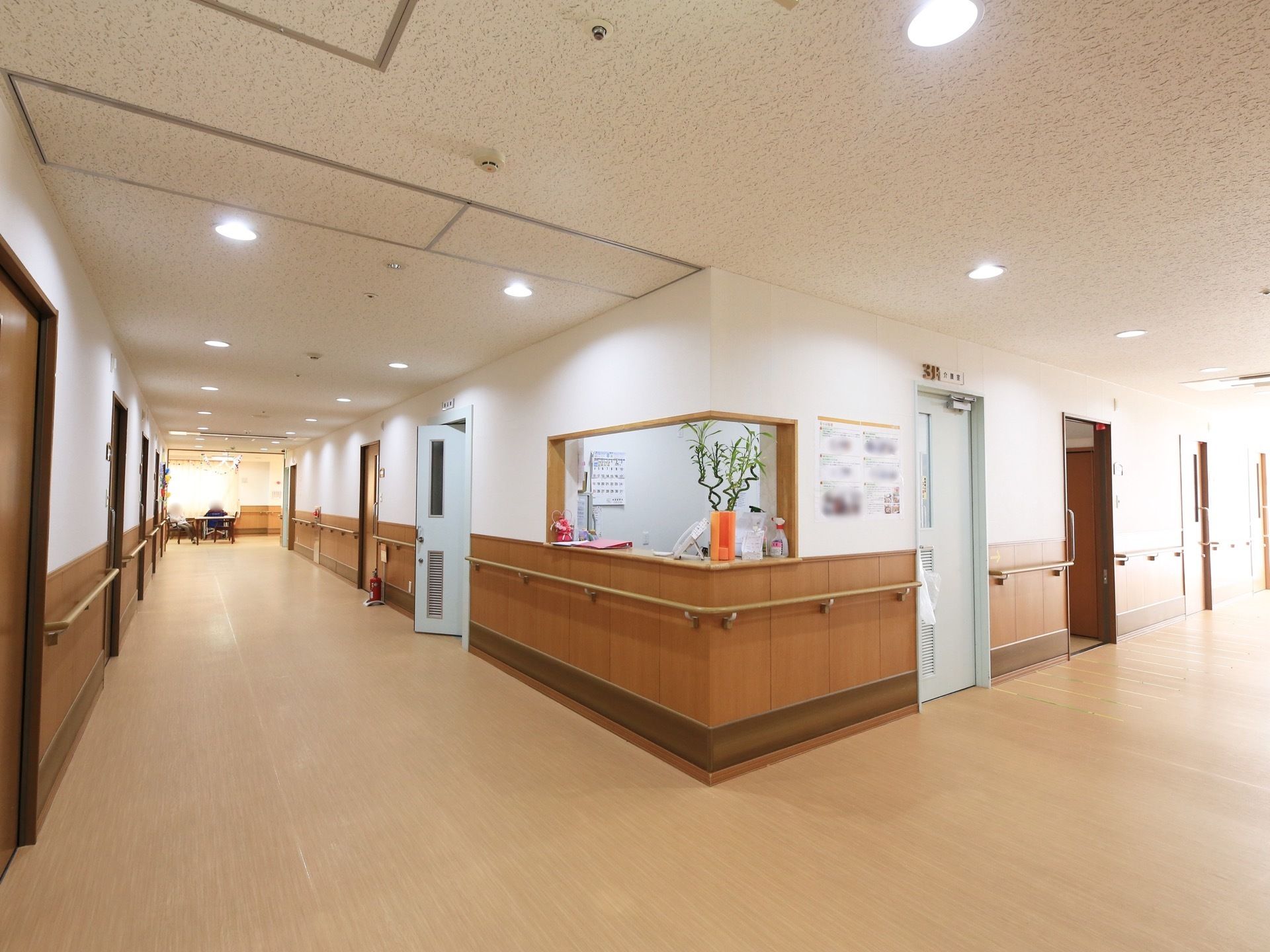 廊下の角に受付があり、隣にスタッフルームになっている。通路は広々と設けられ、車椅子をご利用の方が簡単にすれ違いを行える。