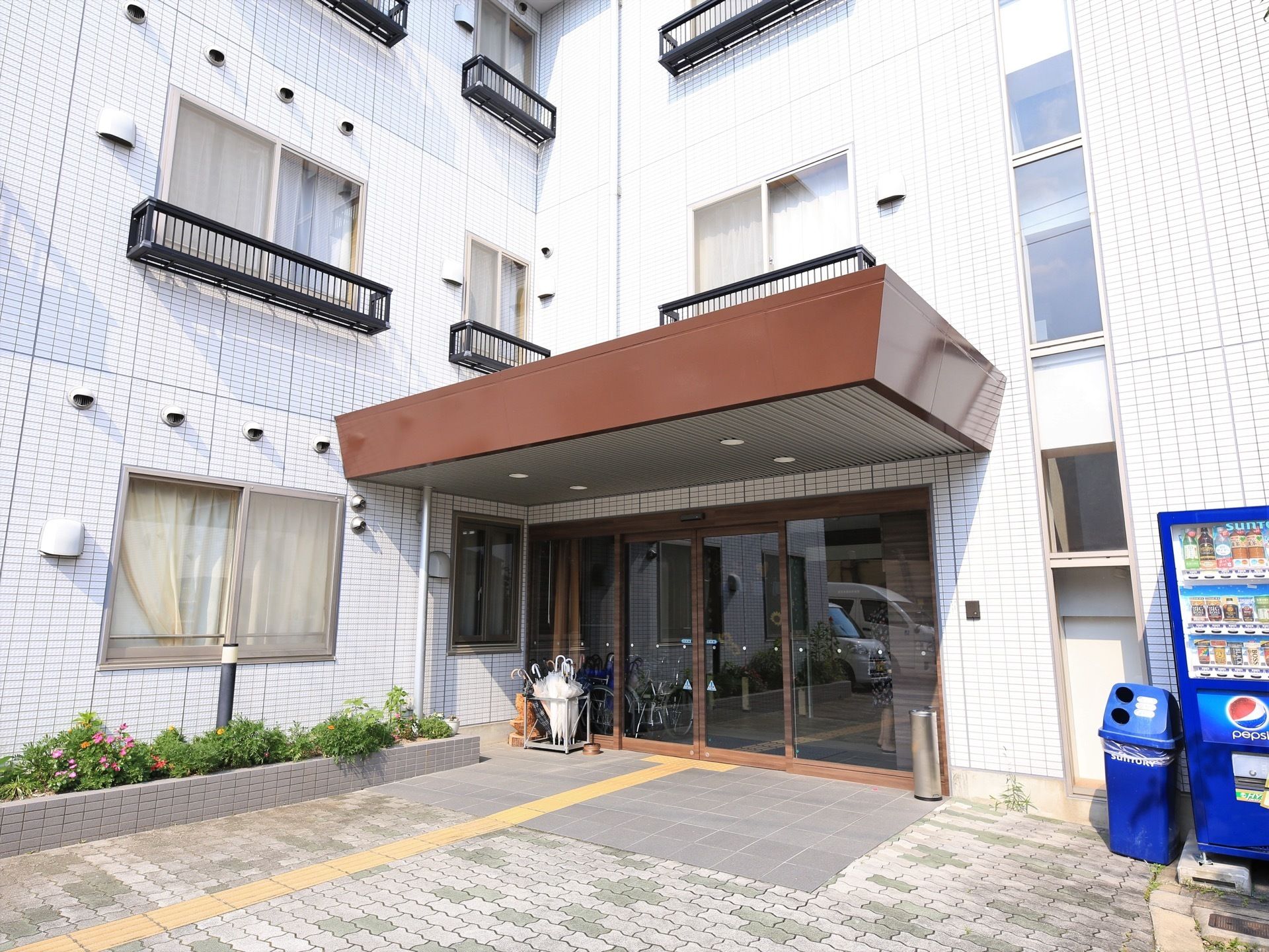 エントランスの周囲には花壇が設置され、色鮮やかな花が育てられている。ドアの傍らに灰皿を設置し、喫煙スペースとなっている。