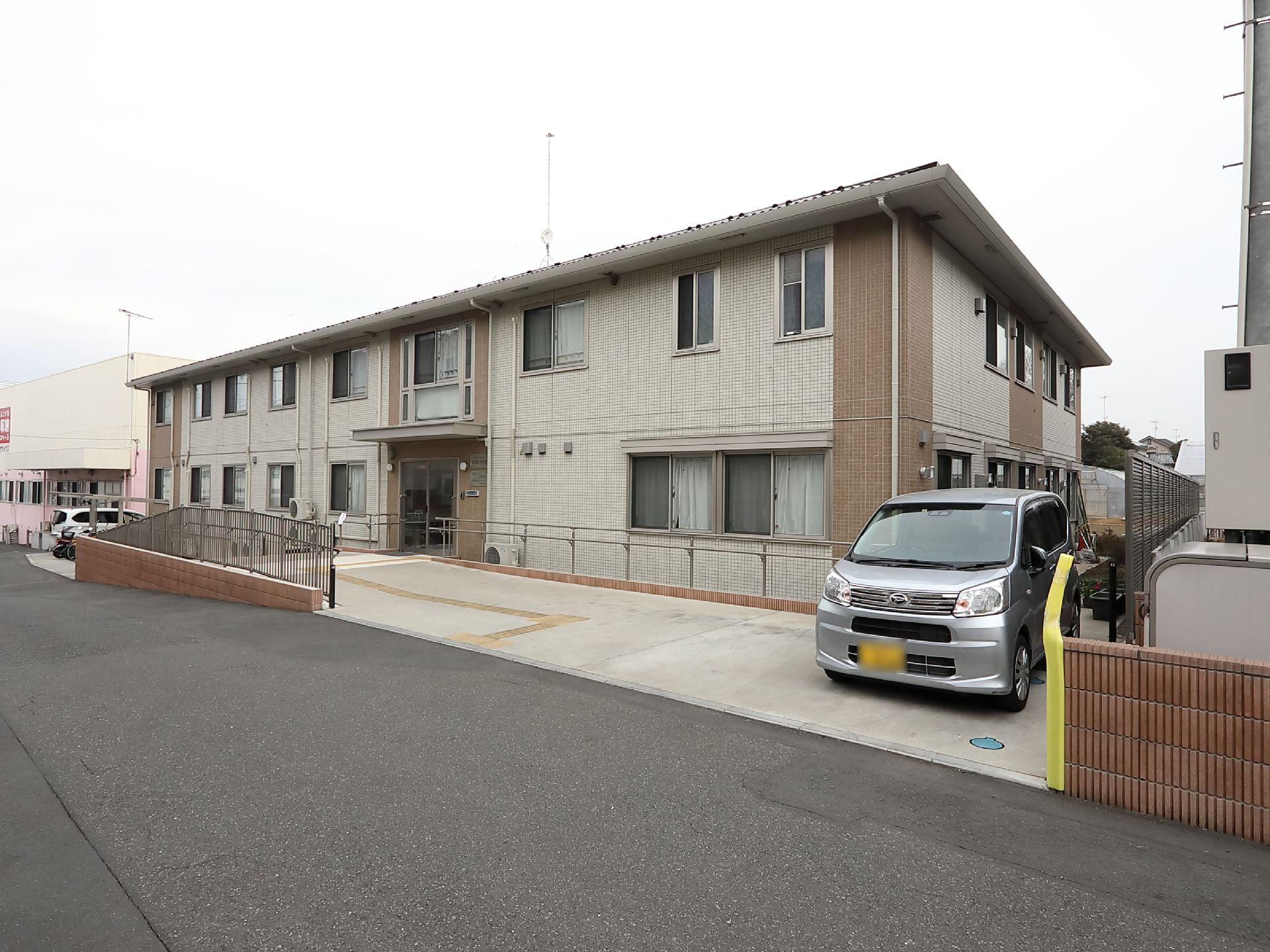 住宅街の中にある広い面積を有したグループホーム。ブラウンとベージュを基調とした落ち着いた色合いの建物である。