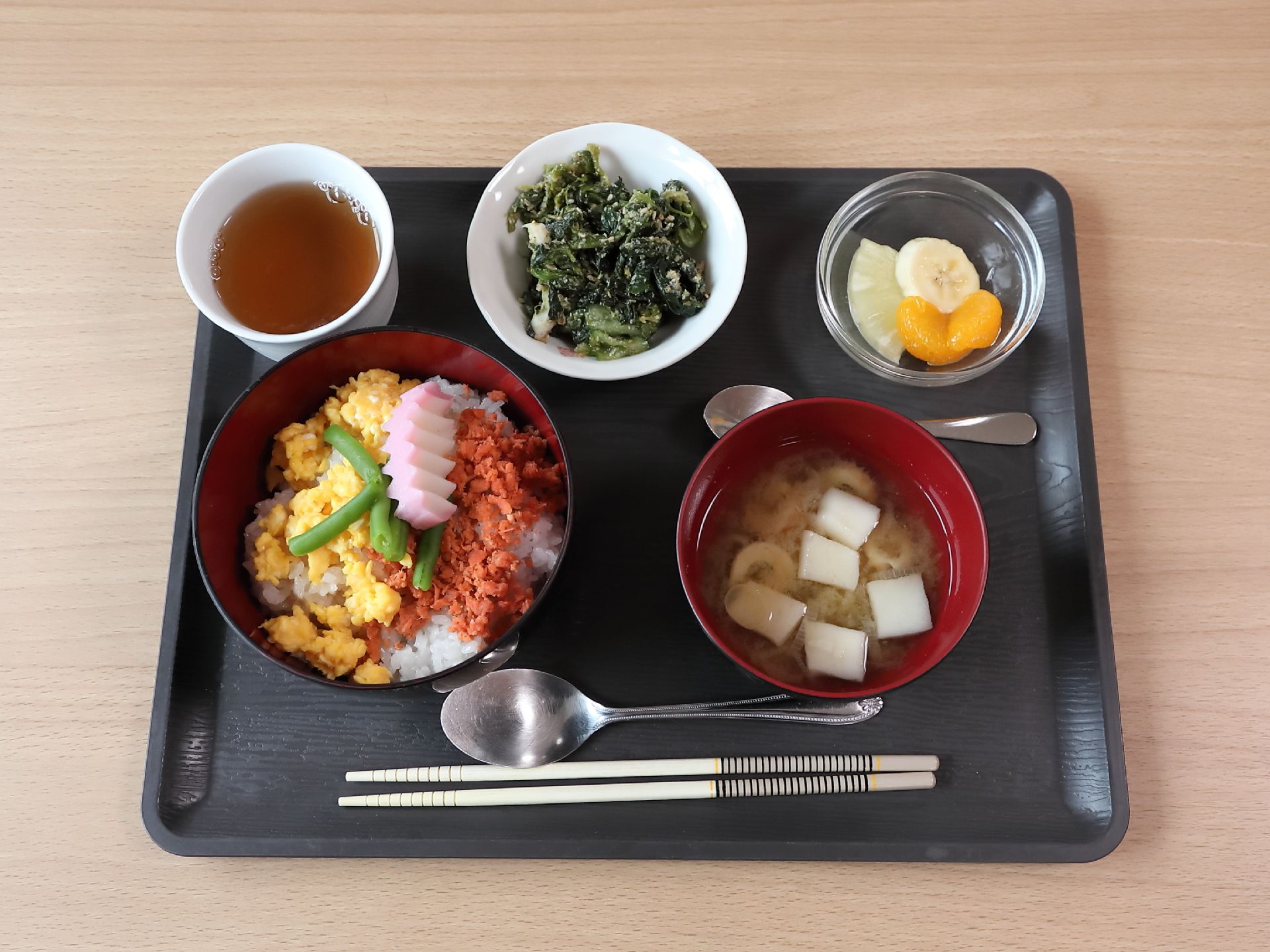 黒いトレーの上に一人前の食事が並べられており、お茶が用意されている。色鮮やかな、目にも楽しいメニューとなっている。