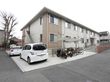 非常階段が設置してある建物で、横に車が２台停められている。屋根付きの駐輪場にはバイクや自転車が複数台置かれている。