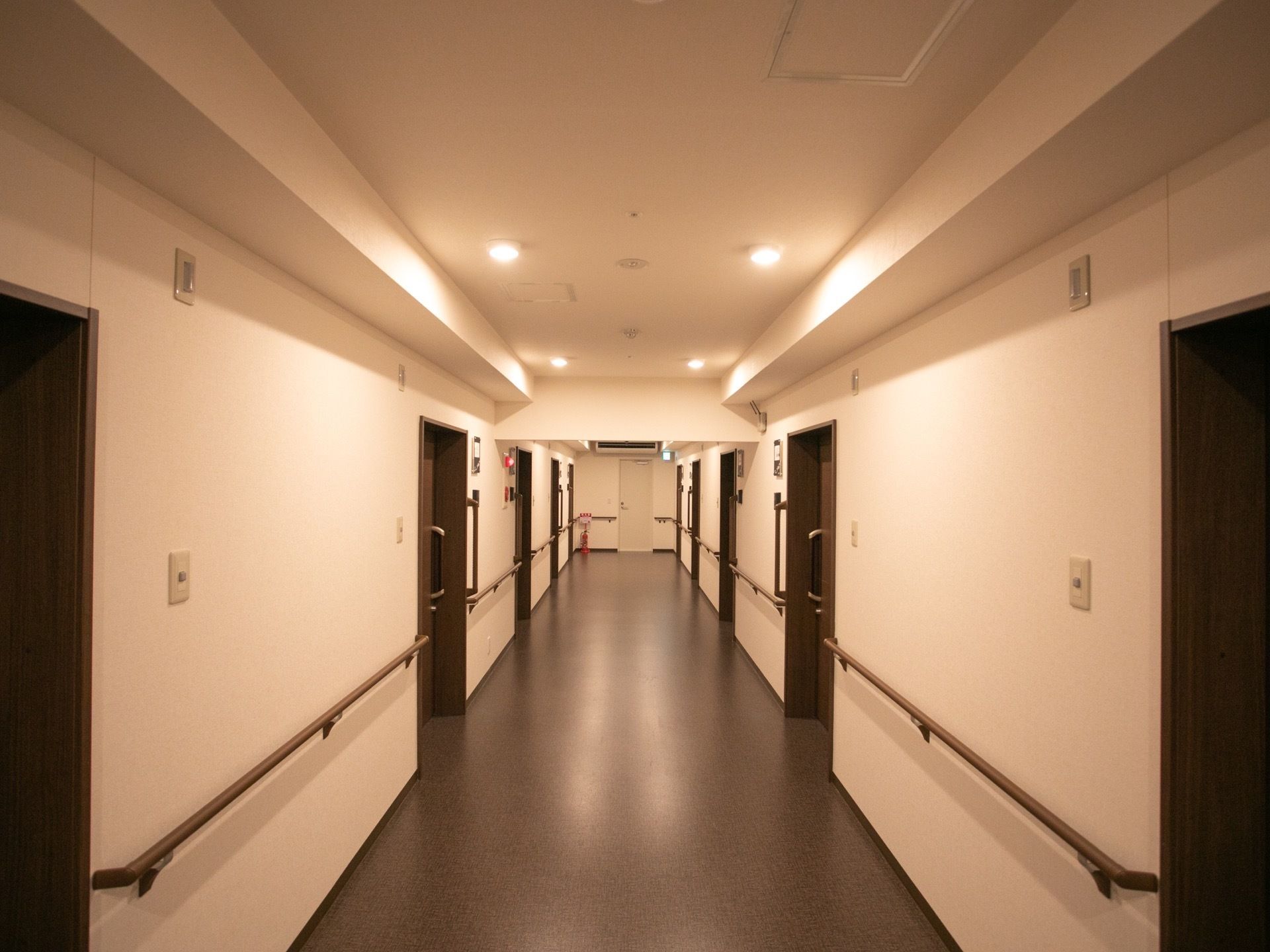 内廊下があり、両側に居室の入り口が並んでいる。天井には照明がついていて、壁には手すりがある。