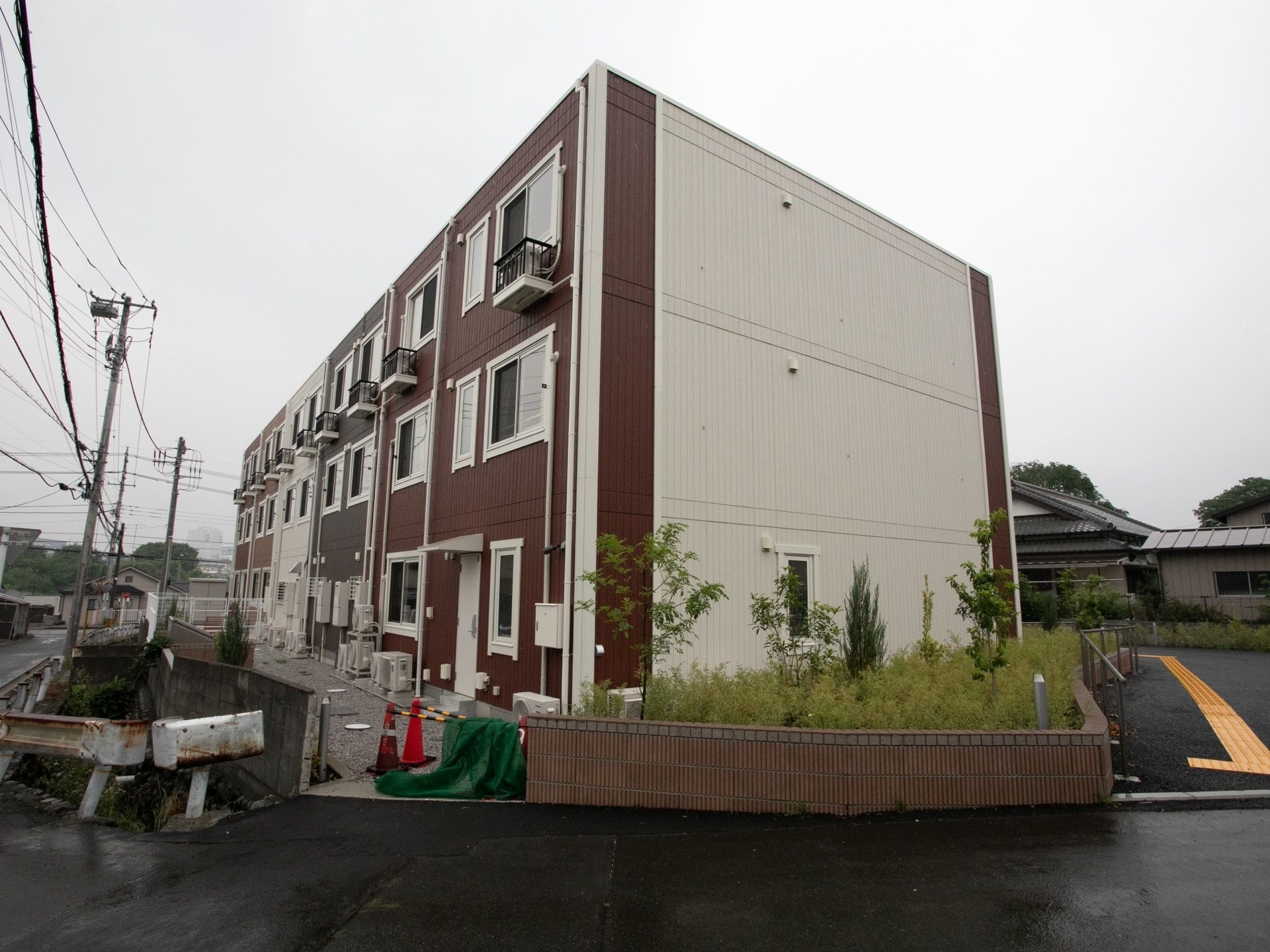 3階建ての建物があり、壁は白や茶色、黒のパネルで彩られている。周辺は戸建ての多い住宅地になっている。