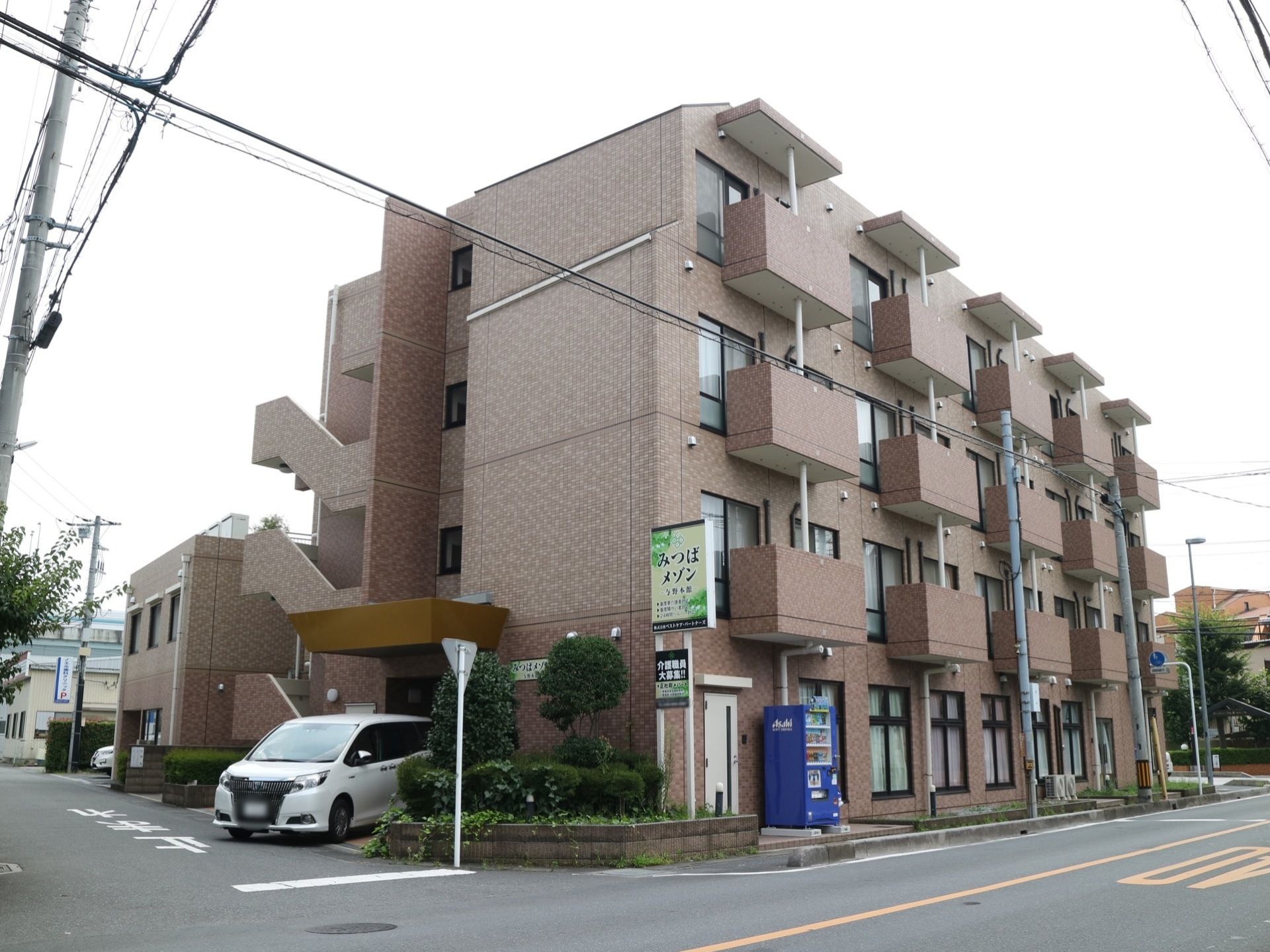 建物の周り、３面は道路に面している。２階以上の屋外には、１室ごとのベランダが見えている。外部には、外階段が設けられている。