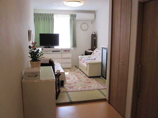 花柄のカーペットやソファ、テレビや収納家具などが置かれた居室。