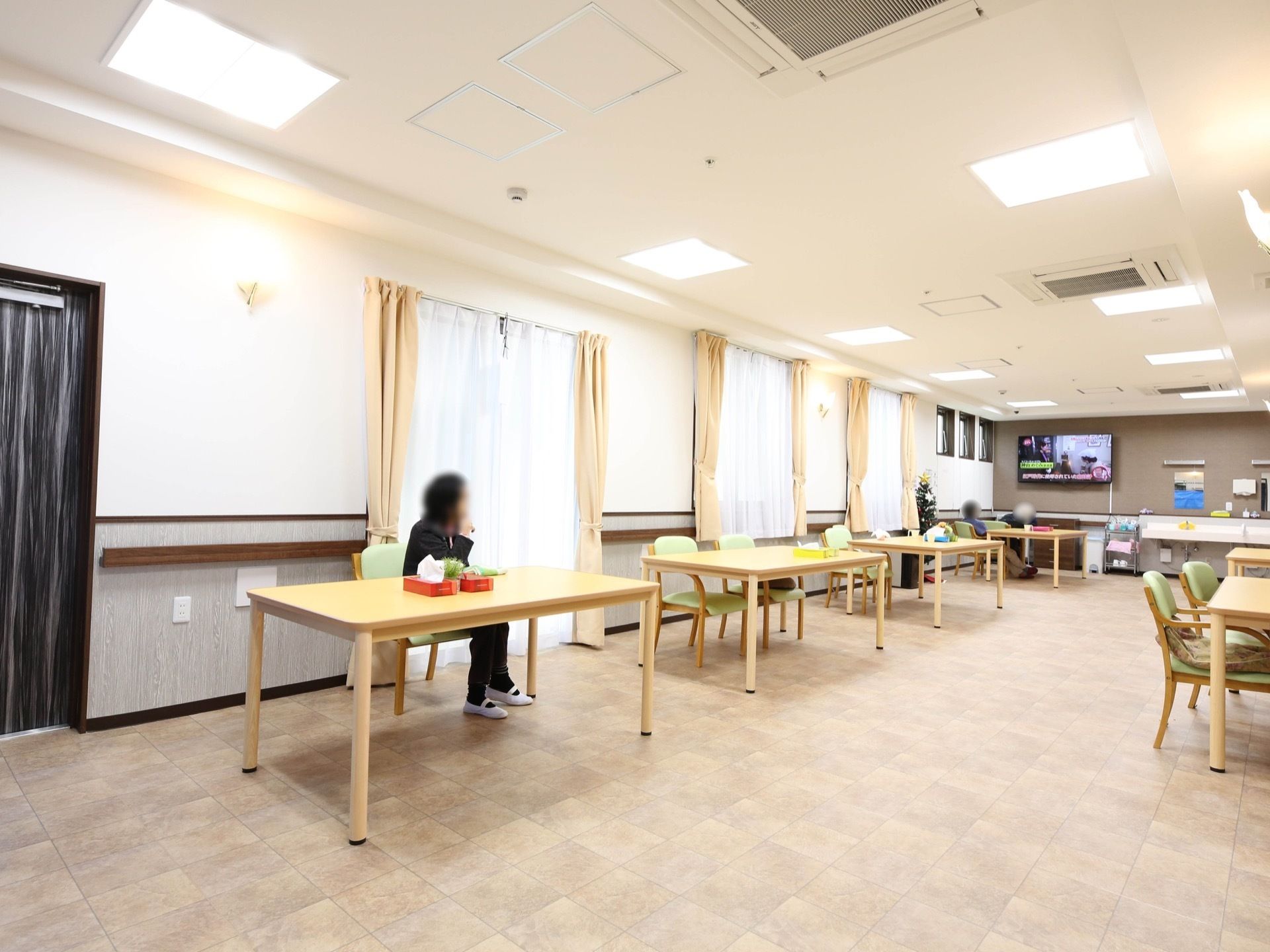 食堂には横並び一直線にテーブルセットが並んでいて、一番奥の壁に壁掛けのテレビが設置されている。入居者様が好きな席に座り、テレビを見ている。