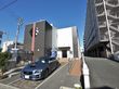 隣に大きいマンションが建っているが、施設の日当たりは良い。玄関前の駐車スペースに車が１台停まっている。