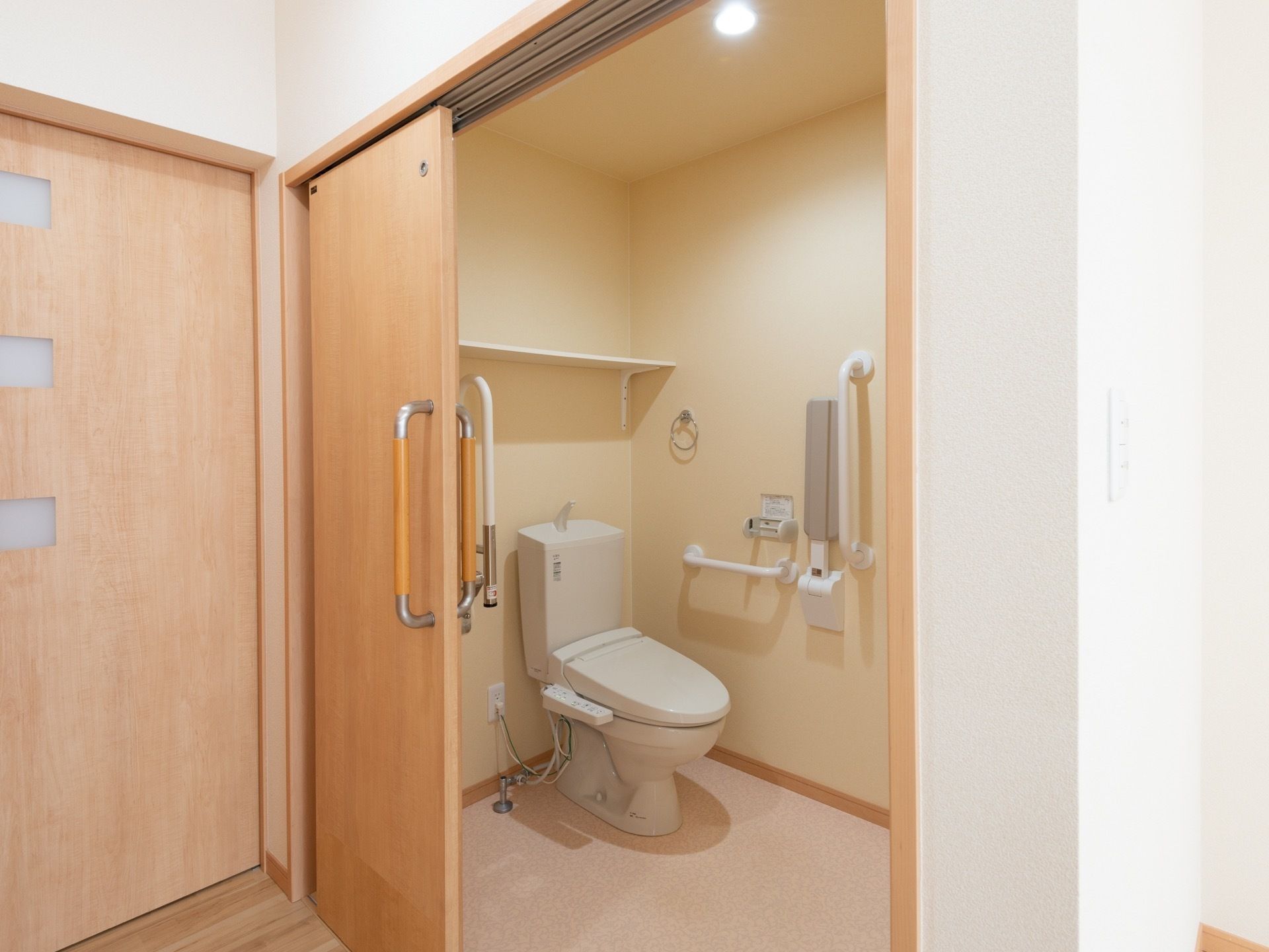 広いスペースのトイレである。温水洗浄便座が設置されている。便座の周囲には随所に手すりが取り付けられている。