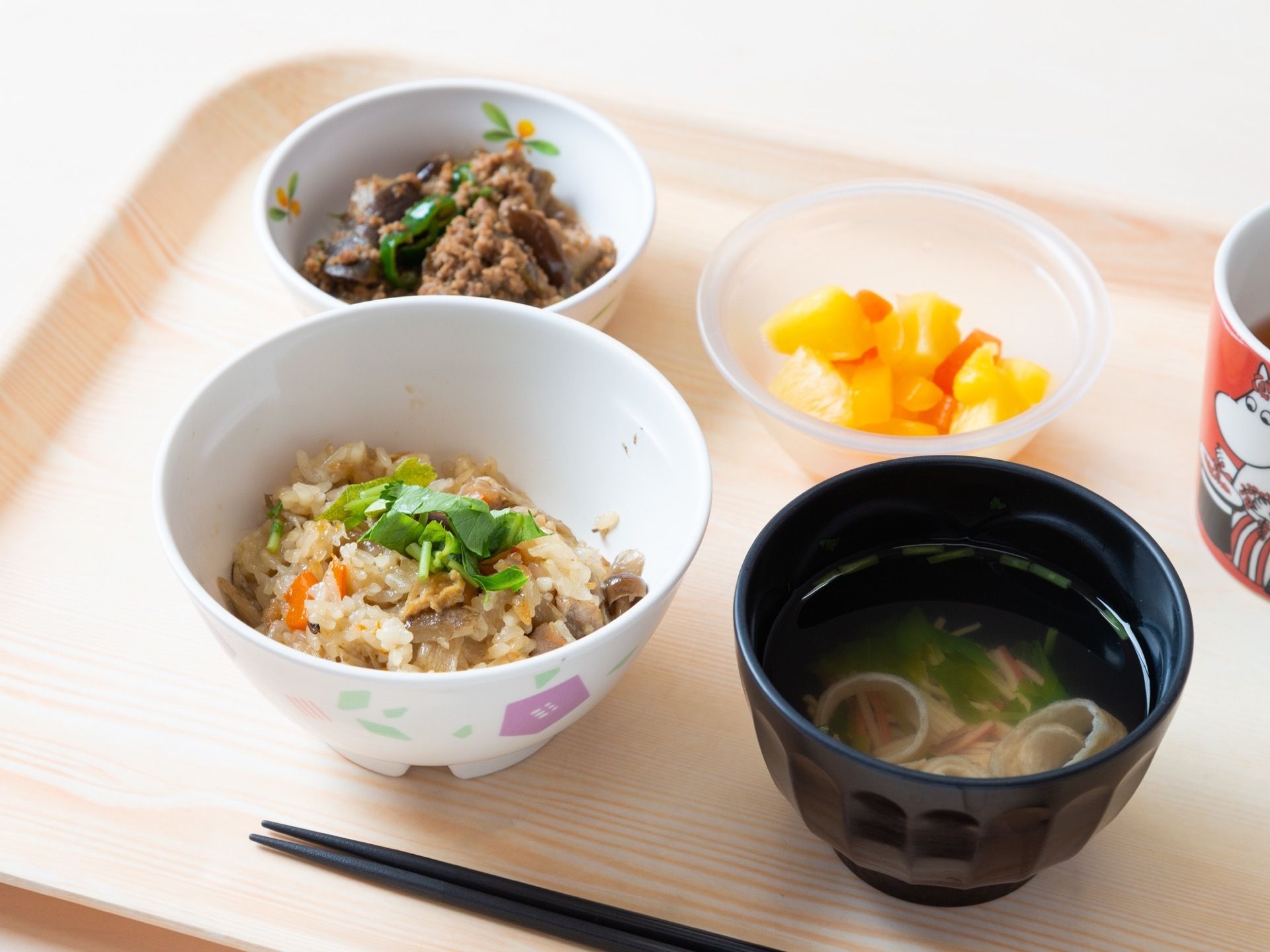 施設で提供される食事メニューの一つである。お盆の上に、そぼろ煮、炊き込みご飯、フルーツ、吸い物、お茶が並んでいる。