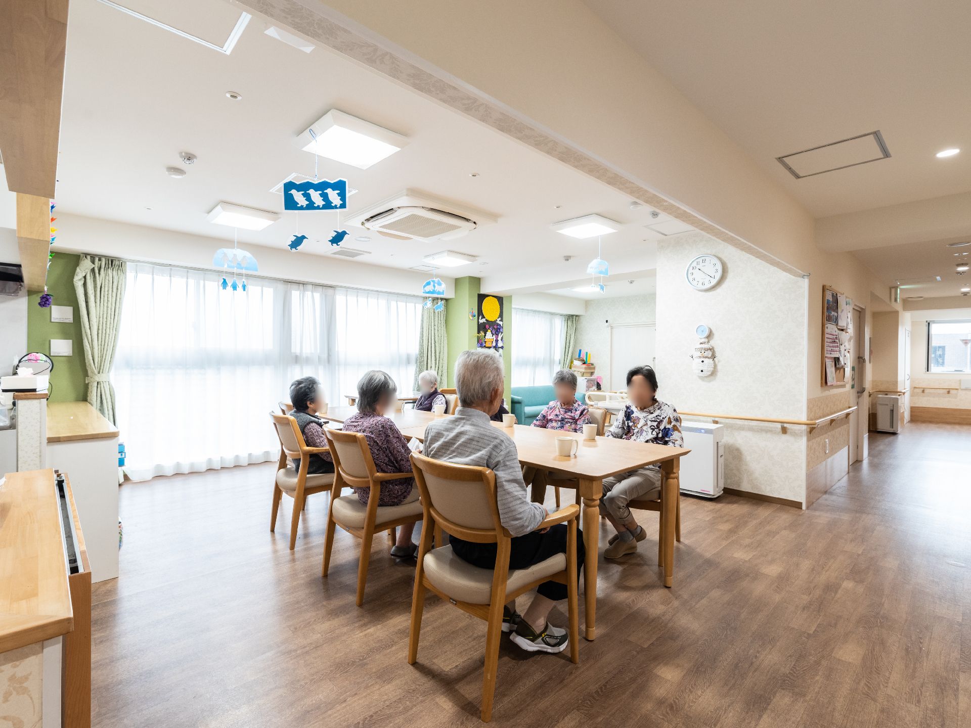 高齢者2名とスタッフが手を握りながら談笑している様子。施設内の会話の一画面