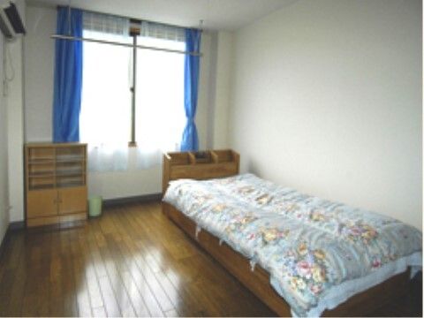 花柄の寝具がセットされたベッドが置かれ、棚などが付いているフローリングの部屋。