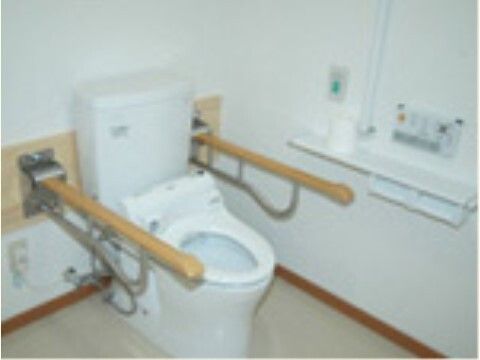 手すりが便座の両サイドに付いたトイレ。壁にも手すりがあり、トイレットペーパーホルダーや呼び出しボタンもある。
