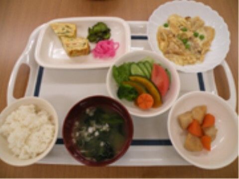 野菜の煮物やサラダ、卵焼きや卵とじのようなものが並べられたトレーには白いご飯とみそ汁もある。