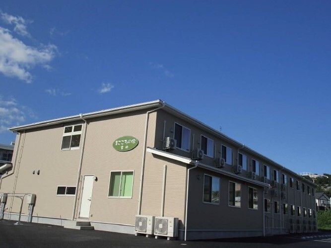 ベージュの外壁の２階建ての建物。窓がたくさん付いていて、外壁には施設名が書かれている。