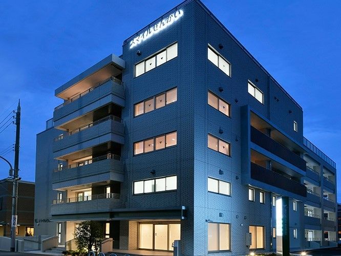 夕暮れ時になりライトアップされた５階建ての建物。明かりが窓から漏れている様子。