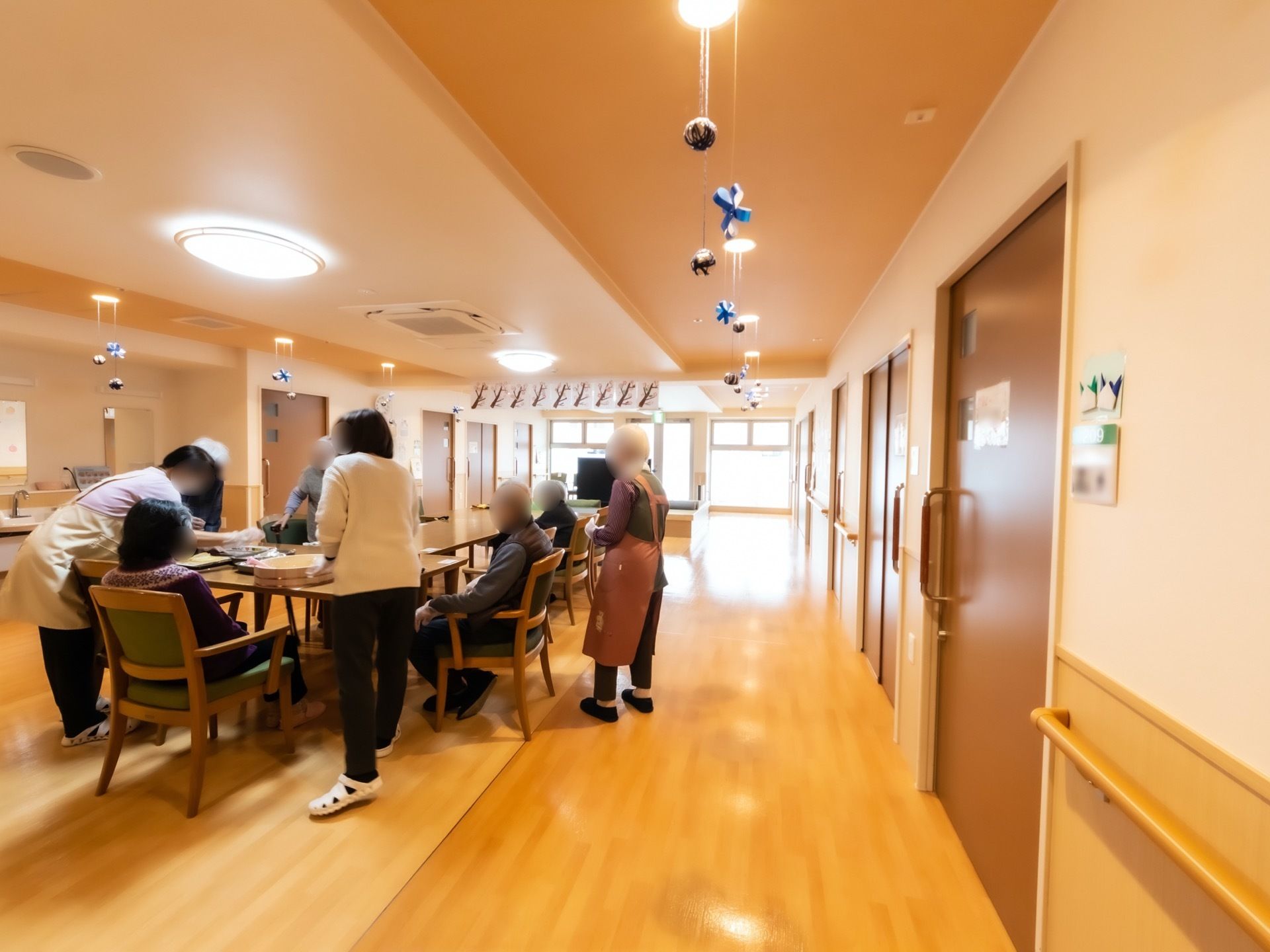 通路途中に設けられている開放的なダイニングで、入居者様やスタッフが集まって作業をしている。天井には装飾が施されている。