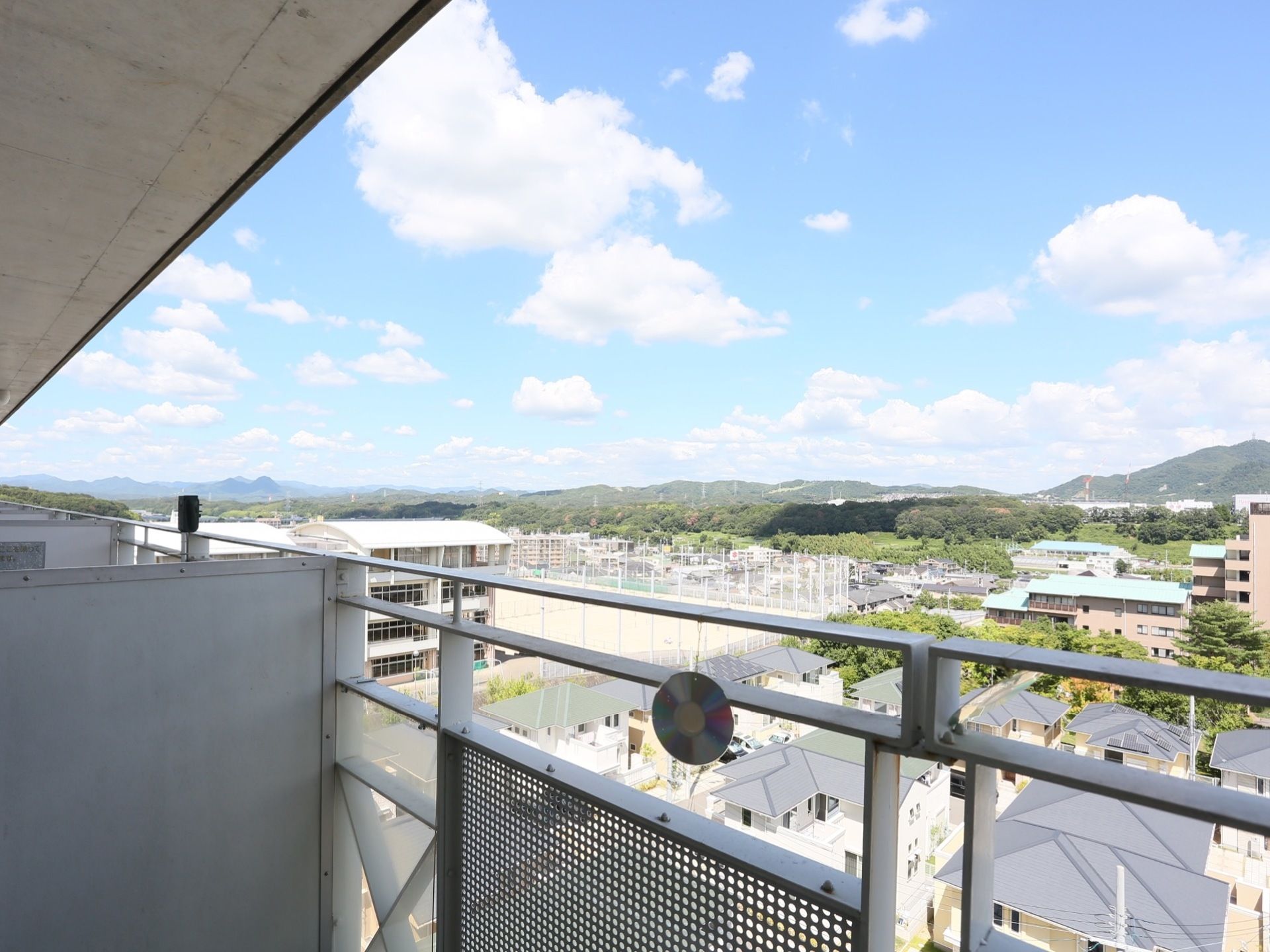 ベランダからは遠くに山並みを望む抜群の眺望が楽しめる。手前には住宅街が広がっていて、学校のような施設が見える。