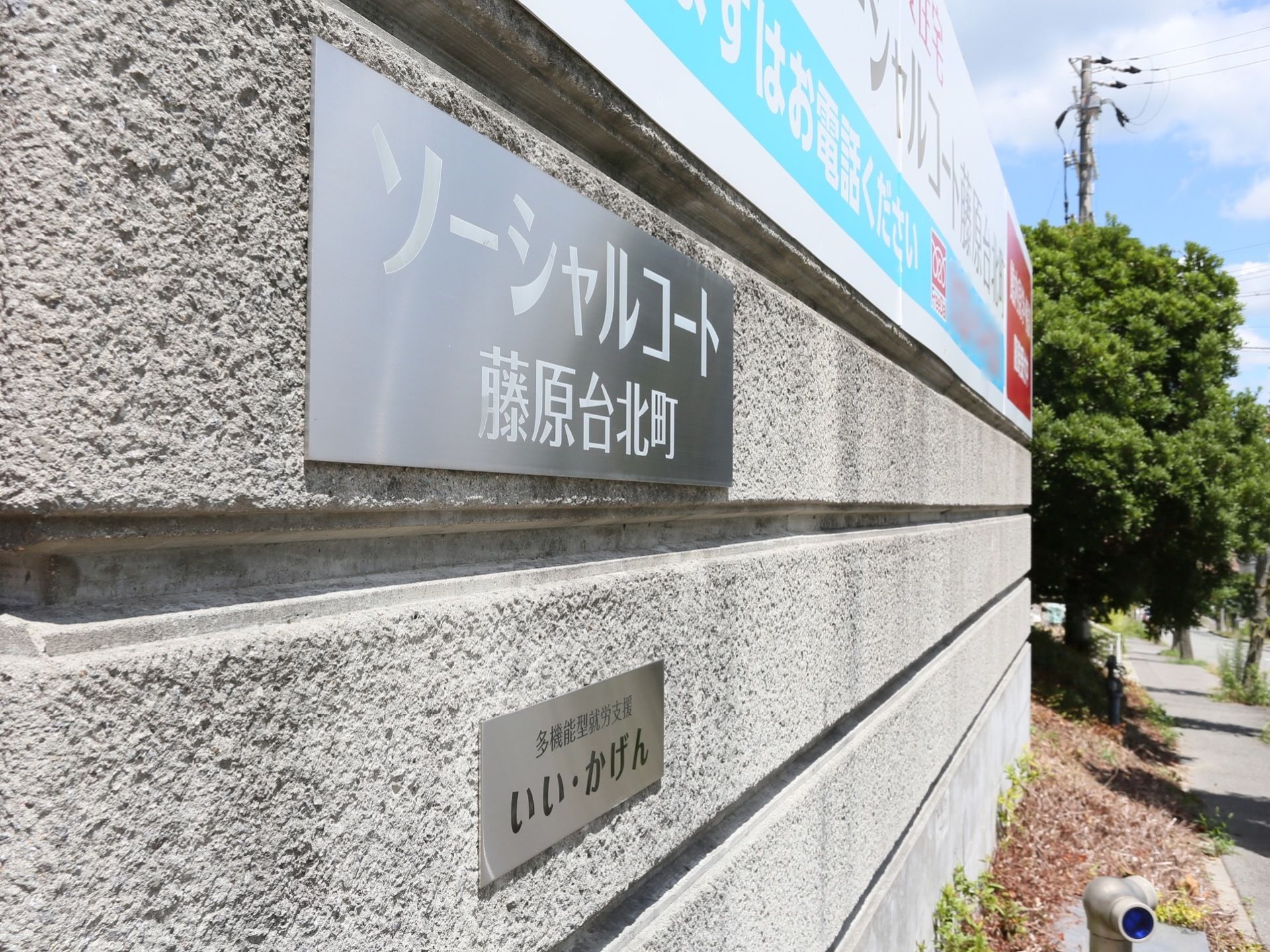コンクリートの壁に銀色をした施設名のプレートが設置されている。その上には施設情報を書いた大きな横断幕が掲げられている。