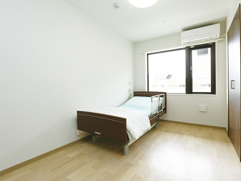 寝具付きのベッドが置かれたフローリングの部屋。ベッドサイドには緊急通報装置が設置されている。