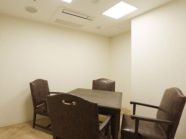 レザー調の椅子が４脚セットされた四角いテーブルが置かれたシンプルな部屋。壁は白く、フロアはフローリング。
