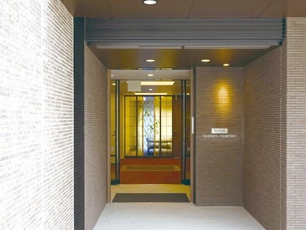 段差のないエントランスにはマットが敷かれ、外壁には住宅名が書かれている。レンガ調の外壁は落ち着いた色合い。