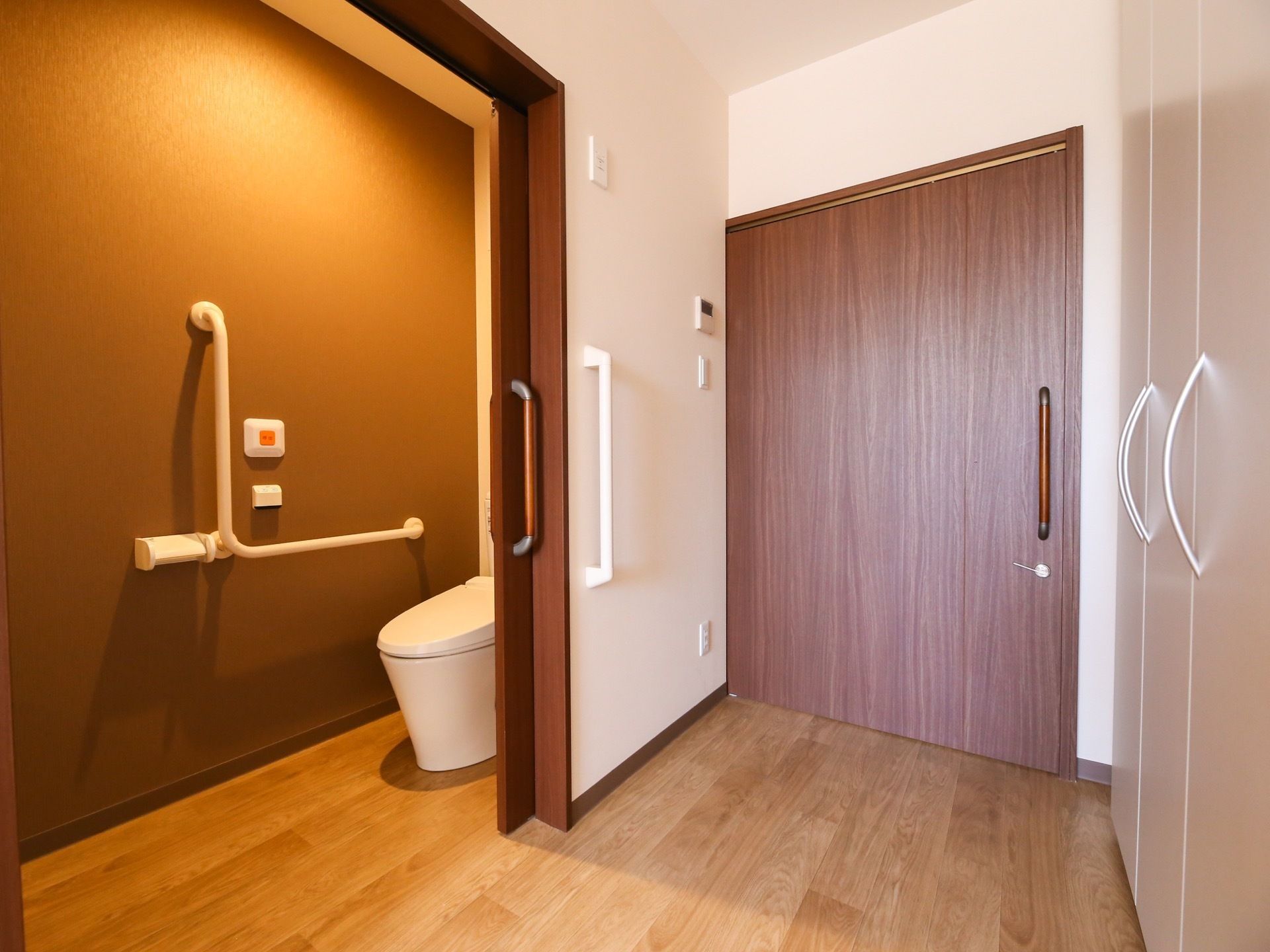 大きな引き戸の居室である。入口付近にトイレがあり、トイレの扉は開いている状態である。中の壁には手すりが取り付けられている。