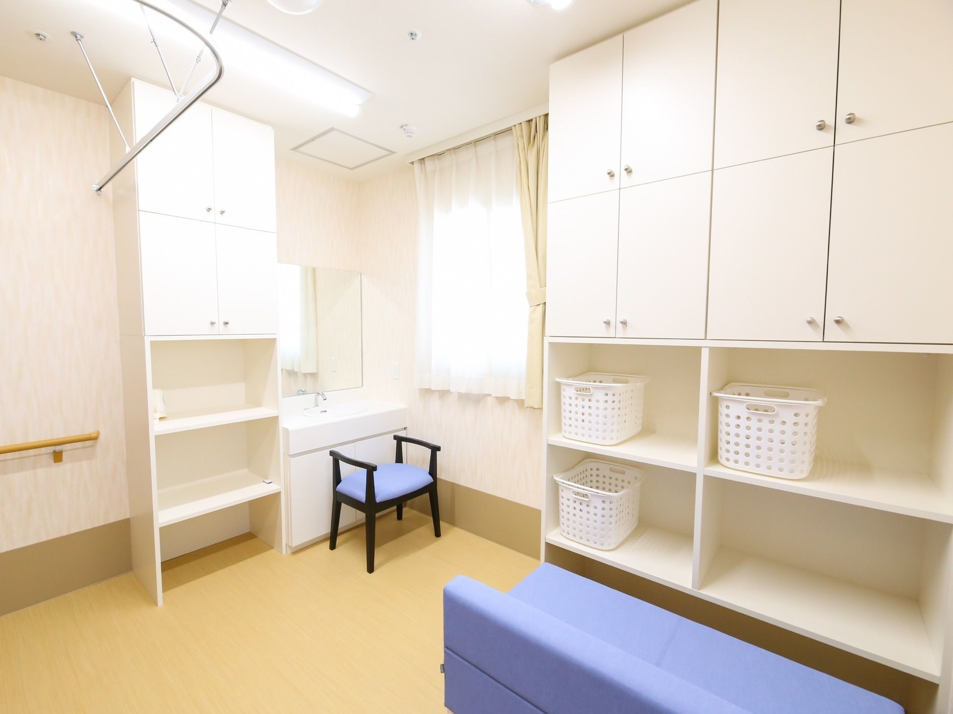 壁面に大きな白い収納棚が設置されており、白いかごが複数置かれている。棚の上部には扉がついている。また、青いソファがある。
