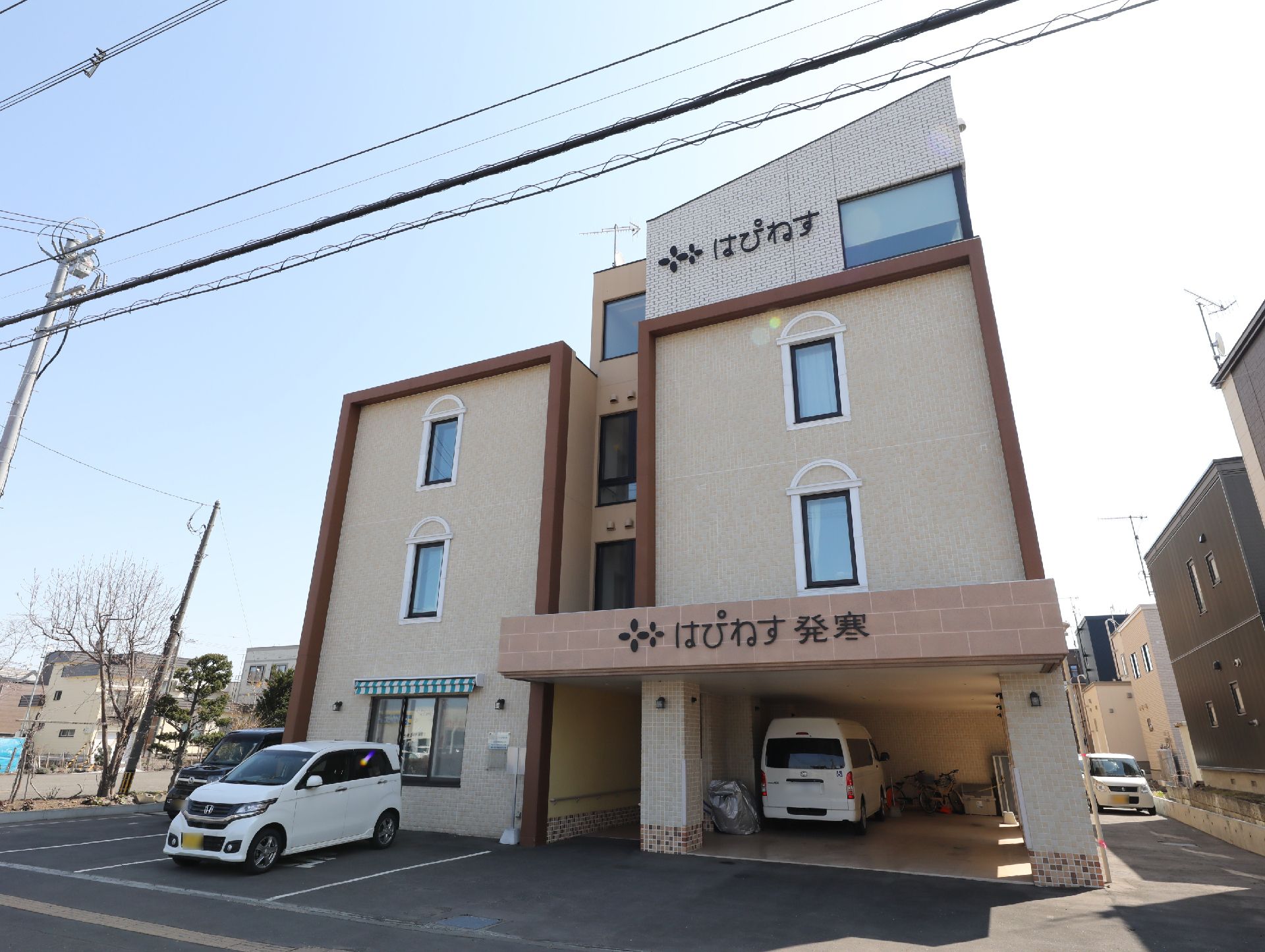 3階建ての建物は日当たりのいい場所に建っている。住宅名が外壁に書かれ、１階部分は駐車場になっている。